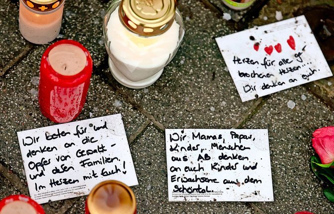 Handgeschriebene Trauerbekundungen liegen neben Trauerkerzen nach dem tödlichen Angriff in Aschaffenburg nahe dem Tatort auf dem Boden.<span class='image-autor'>Foto: dpa/Daniel Löb</span>