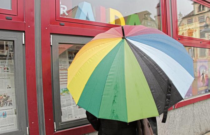 In dieser Kombination hat schlechte Laune auch bei Regen keine Chance: mit einem farbenfrohen Schirm in der Hand die Heimatzeitung lesen und sich vor dem Reisebüro an wärmere Orte denken. So lässt sich das Wetter aushalten.  Foto: Rostek