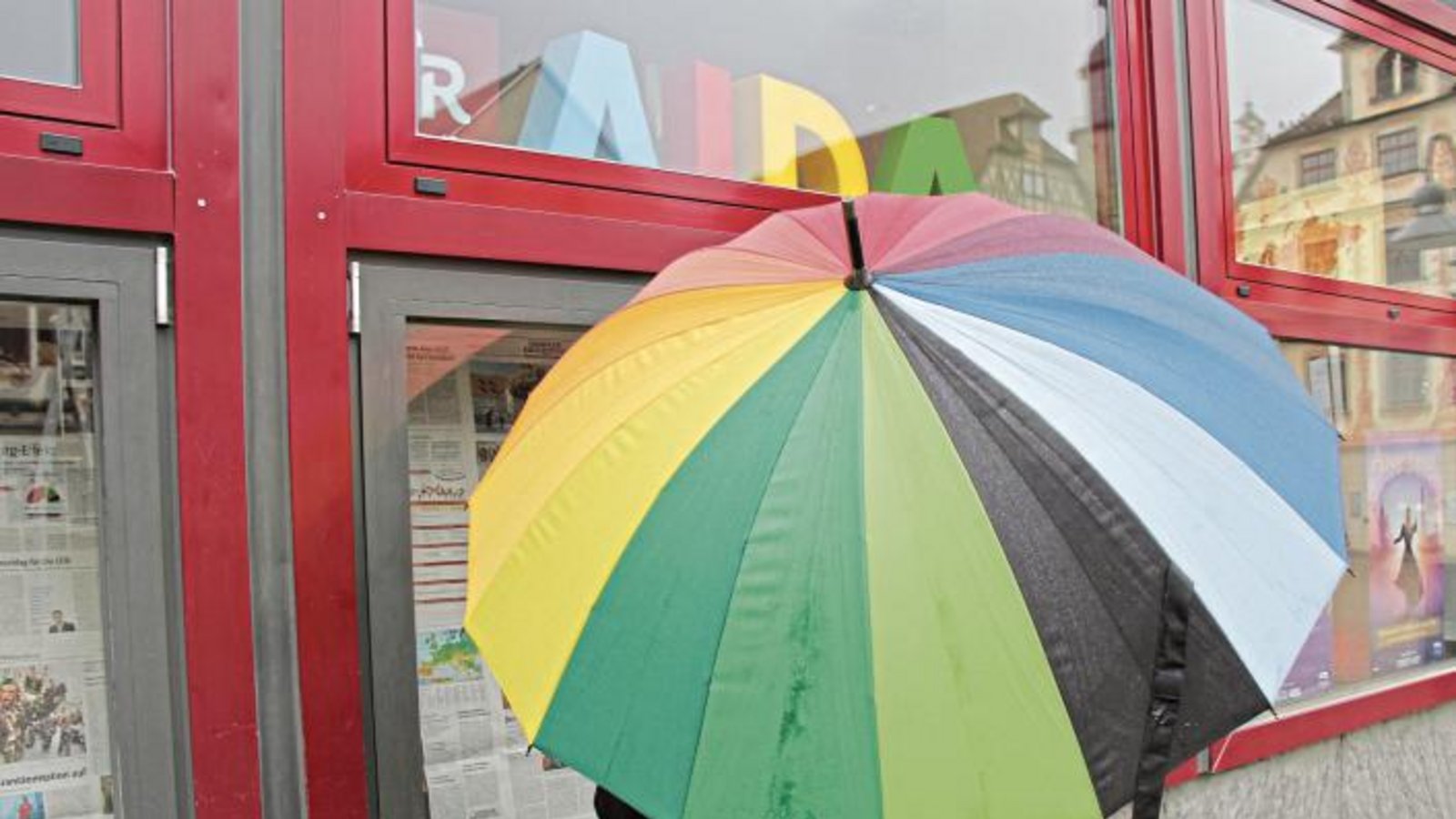 In dieser Kombination hat schlechte Laune auch bei Regen keine Chance: mit einem farbenfrohen Schirm in der Hand die Heimatzeitung lesen und sich vor dem Reisebüro an wärmere Orte denken. So lässt sich das Wetter aushalten. Foto: Rostek In dieser Kombination hat schlechte Laune auch bei Regen keine Chance: mit einem farbenfrohen Schirm in der Hand die Heimatzeitung lesen und sich vor dem Reisebüro an wärmere Orte denken. So lässt sich das Wetter aushalten. Foto: Rostek