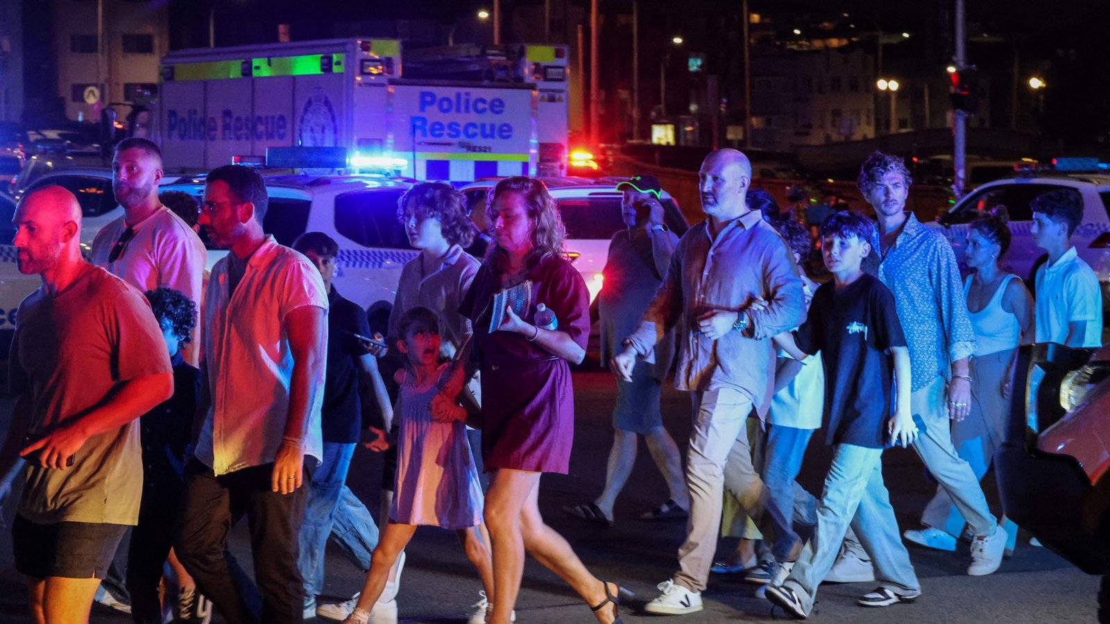 Menschen überqueren eine Straße neben Polizeifahrzeugen nach einem Schusswaffenangriff am Bondi Beach in Sydney am 14. Dezember 2025.Foto: DAVID GRAY / AFP