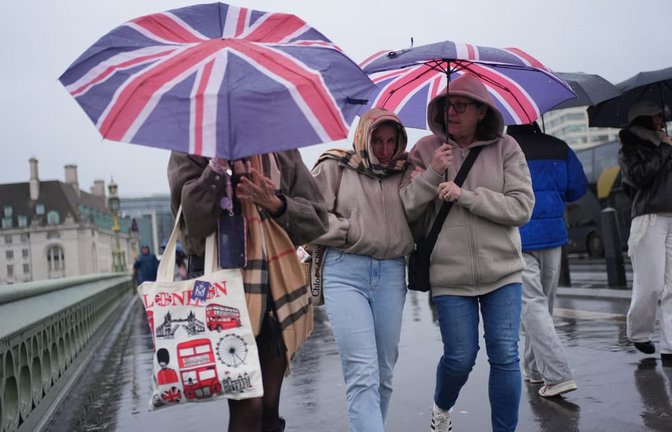 Menschen im Regen auf der Westminster Bridge in London.<span class='image-autor'>Yui Mok/PA Wire/dpa</span>