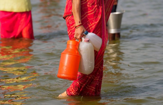 Eine Hinduistin geht nach dem Wasserholen mit Kunststoffkanistern im Sangam, dem Zusammenfluss des Ganges und Yamuna.<span class='image-autor'>Foto: Rajesh Kumar Singh/AP</span>