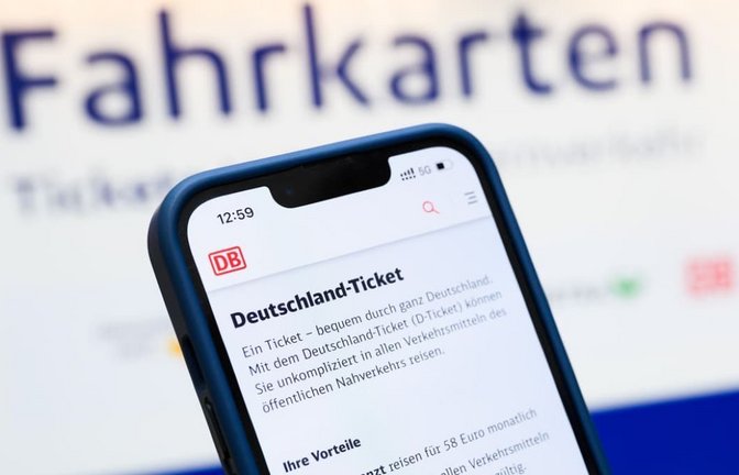 Eine Person hält ein Smartphone in der Hand, auf dessen Display eine Information zum Kauf des Deutschlandtickets zu sehen ist, während sie vor einem Fahrkartenautomaten steht.<span class='image-autor'>Julian Stratenschulte/dpa</span>