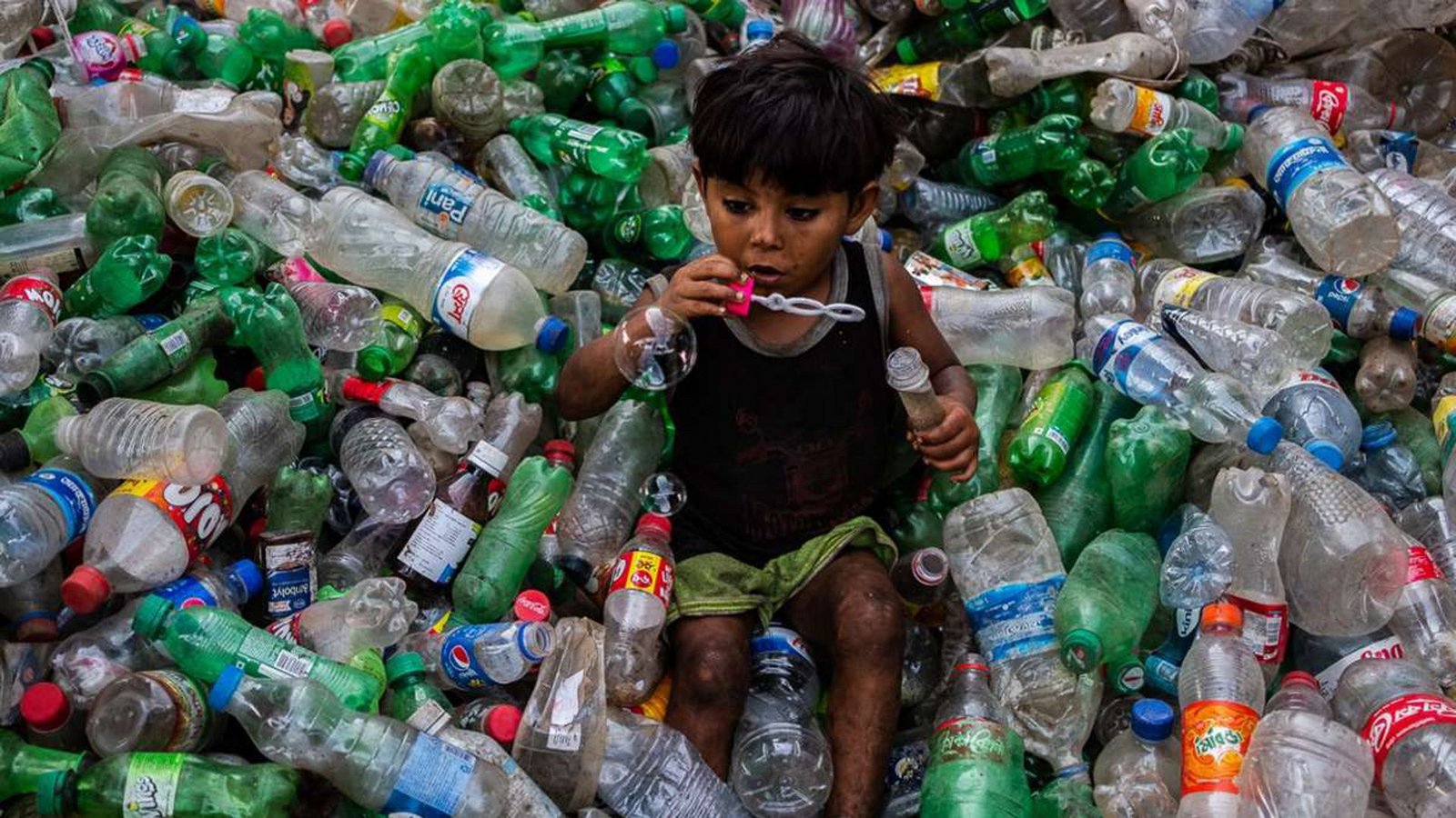 Ein Junge pustet Seifenblasen auf einem Stapel von Plastikflaschen in einer Recycling-Anlage in Dhaka (Bangladesch).Foto: Nayem Shaan/ZUMA Wire/dpa Ein Junge pustet Seifenblasen auf einem Stapel von Plastikflaschen in einer Recycling-Anlage in Dhaka (Bangladesch).Foto: Nayem Shaan/ZUMA Wire/dpa