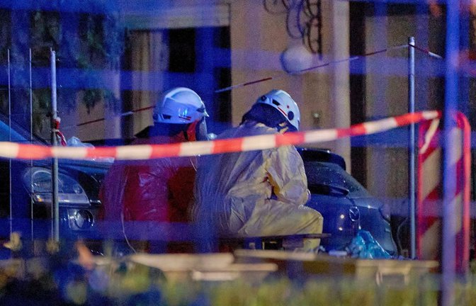 Einsatztkräfte in Schutzanzügen und mit Gasmasken sitzen im hessichen Runkel hinter einer Absperrung.<span class='image-autor'>Foto: Sascha Ditscher/dpa</span>