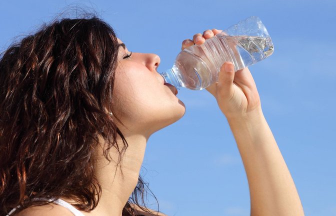 Profil einer Frau, die Wasser aus einer Plastikflasche trinkt. Im Hintergrund ist ein blauer Himmel zu sehen (Symbolfoto).<span class='image-autor'>Foto: IMAGO/Design Pics/IMAGO</span>