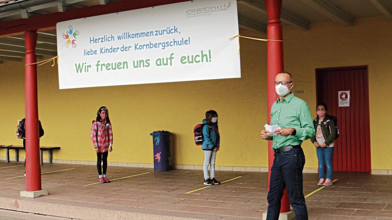 Die Kinder stehen an der Kornbergschule einzeln und mit Mund-Nasen-Schutz an Markierungen und warten auf den Eintritt ins Schulgebäude.  Fotos: Rücker