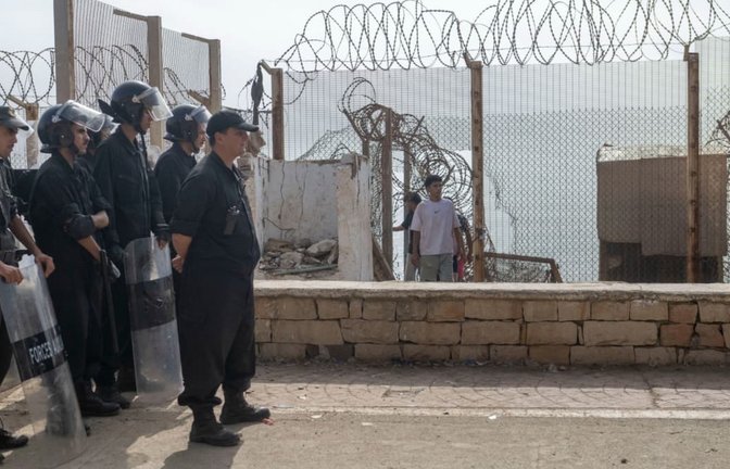 Marokkanische Sicherheitskräfte stehen neben einem durchbrochenen Stacheldrahtzaun Wache, während Menschen, die versucht hatten, nach Ceuta, Spanien, zu gelangen, in die nordmarokkanische Stadt Fnideq zurückkehren (Archivfoto).<span class='image-autor'>STR/AP/dpa</span>