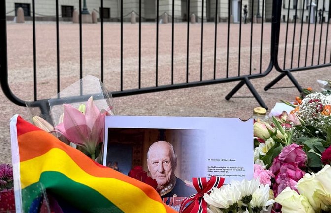 Eine Regenbogenfahne und ein Porträt des verstorbenen Königs Harald V. liegen vor dem Königlichen Schloss Oslo, wo zahlreiche Menschen zusammengekommen sind um zu trauern.<span class='image-autor'>Julia Wäschenbach/dpa</span>