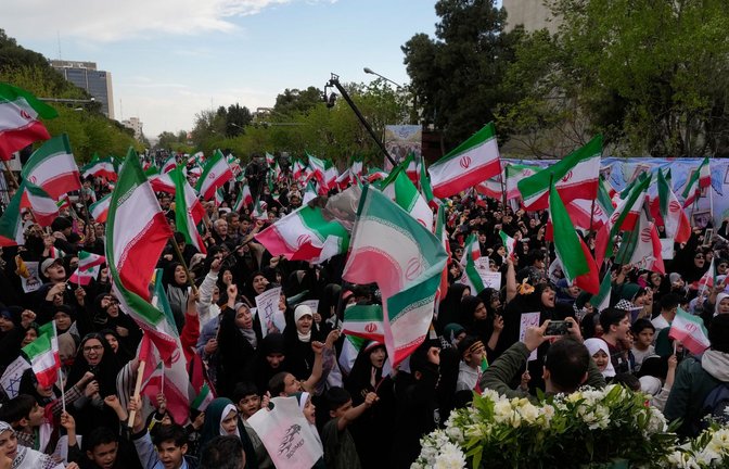 Menschen schwenken iranische Fahnen bei einer Gedenkfeier für Schulkinder, die am 28. Februar bei einem US-Luftangriff auf eine Schule in  Minab getötet wurden.<span class='image-autor'>Foto: Vahid Salemi/AP/dpa/Vahid Salemi</span>