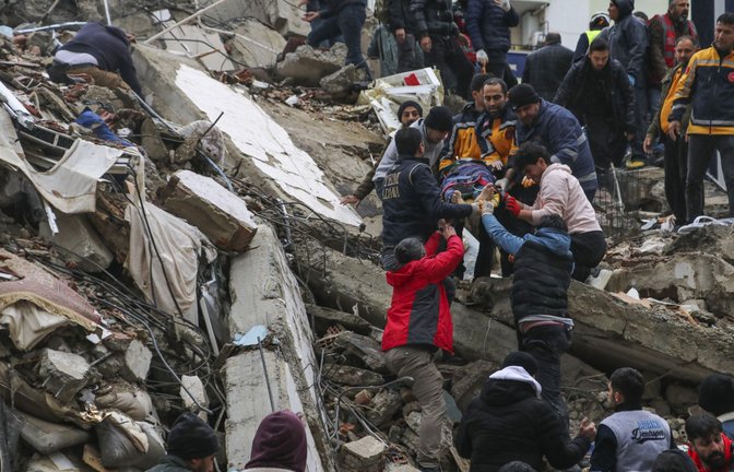 Menschen und Rettungskräfte bergen in der türkischen Stadt Adana eine Person auf einer Bahre aus einem eingestürzten Gebäude. Ein starkes Beben hat im Südosten der Türkei und in Syrien mehrere Gebäude zum Einsturz gebracht, und es werden viele hundert Opfer befürchtet.<span class='image-autor'>Foto: Elifaysenurbay/IHA/AP//pa</span>