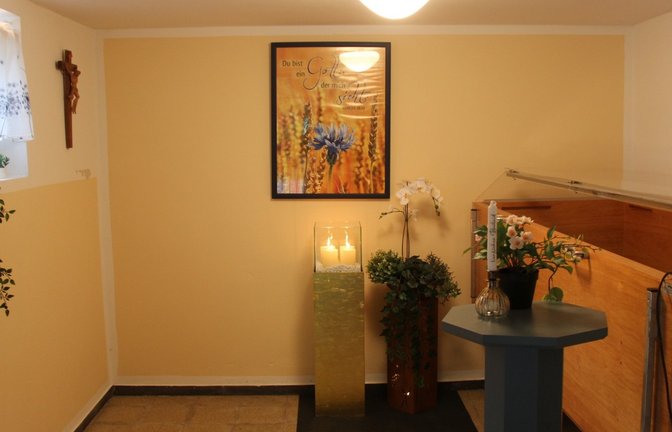 Warme Farben: Zwei Wände sind sandfarben gestrichen, Kerzen und Kunstblumen neu hinzugekommen. Links steht üblicherweise ein Bett, auf dem der Leichnam aufgebahrt wird.