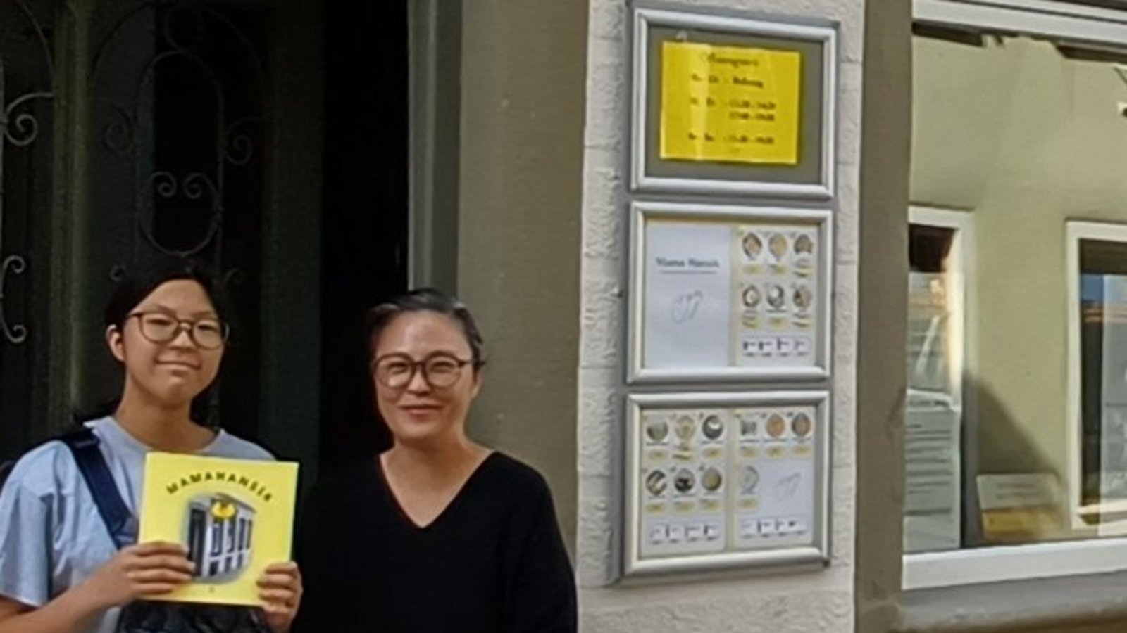 Jihyun Han (rechts) vor dem Mamahansik, ihre Tochter Seoin zeigt das Buch über den Imbiss.