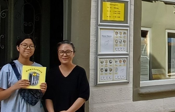 Jihyun Han (rechts) vor dem Mamahansik, ihre Tochter Seoin zeigt das Buch über den Imbiss.