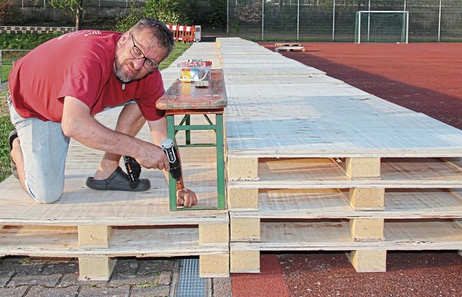 Rund 30 Meter lang steht die Palettentribüne auf dem Hartplatz oberhalb des Rasenplatzes am Alten Postweg. Helmut Modenese befestigt nun noch Bierbänke als Sitzgelegenheit. Fotos: Nachreiner