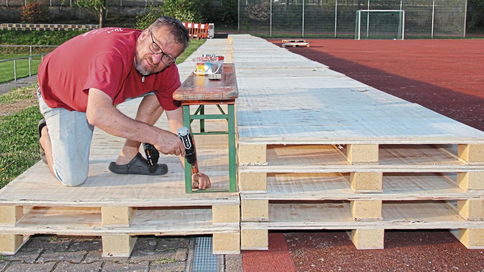 Rund 30 Meter lang steht die Palettentribüne auf dem Hartplatz oberhalb des Rasenplatzes am Alten Postweg. Helmut Modenese befestigt nun noch Bierbänke als Sitzgelegenheit. Fotos: Nachreiner Rund 30 Meter lang steht die Palettentribüne auf dem Hartplatz oberhalb des Rasenplatzes am Alten Postweg. Helmut Modenese befestigt nun noch Bierbänke als Sitzgelegenheit. Fotos: Nachreiner
