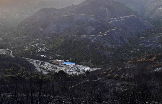Nach einem Waldbrand umgeben verkohlte Berge ein Dorf im Tal.<span class='image-autor'>Fateh Guidoum/AP/dpa</span>