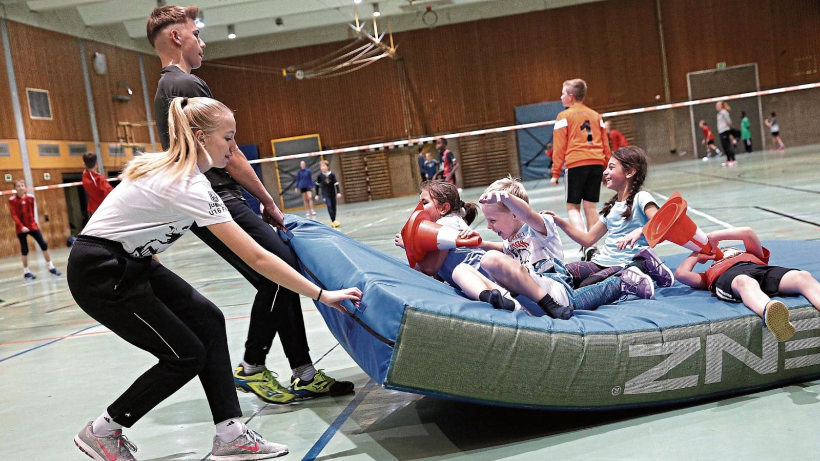 Fröhliche Kinder, fröhliche Betreuer: Wenn Lena und Jan Schiller die Matten zurückziehen, nutzen einige Kinder aus der TVV-Ballschule dies als Mitfahrgelegenheit. Fotos: Küppers Fröhliche Kinder, fröhliche Betreuer: Wenn Lena und Jan Schiller die Matten zurückziehen, nutzen einige Kinder aus der TVV-Ballschule dies als Mitfahrgelegenheit. Fotos: Küppers