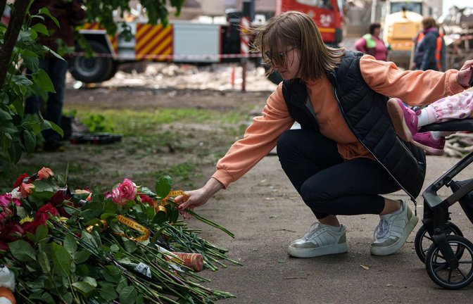 Eine Frau legt Blumen vor einem Haus ab, das nach einem russischen Angriff schwer beschädigt wurde. Nach Angaben von „Save the Children“ sind bislang mehr als 3.500 Kinder  in der Ukraine gestorben. (Archivfoto).<span class='image-autor'>Foto: Evgeniy Maloletka/AP/dpa/Evgeniy Maloletka</span>