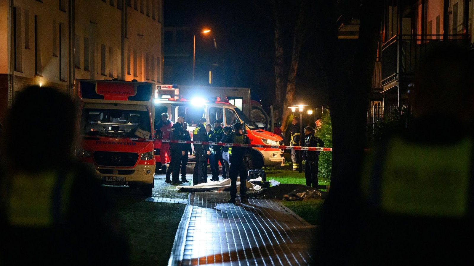 Polizisten, Ermittler und Rettungskräfte stehen am Tatort neben zwei abgedeckten Leichen.Foto: Jonas Walzberg/dpa