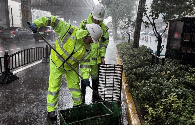 Arbeiter reinigen einen Abflussrost auf einer Straße im Bezirk Xuhui. Shanghai wurde am Sonntag von starken Winden und Regenfällen heimgesucht, als sich der Taifun „Dolphin“ näherte; die Auswirkungen des Taifuns werden voraussichtlich bis zum 11. August andauern.<span class='image-autor'>Wei Qingfeng/XinHua/dpa</span>