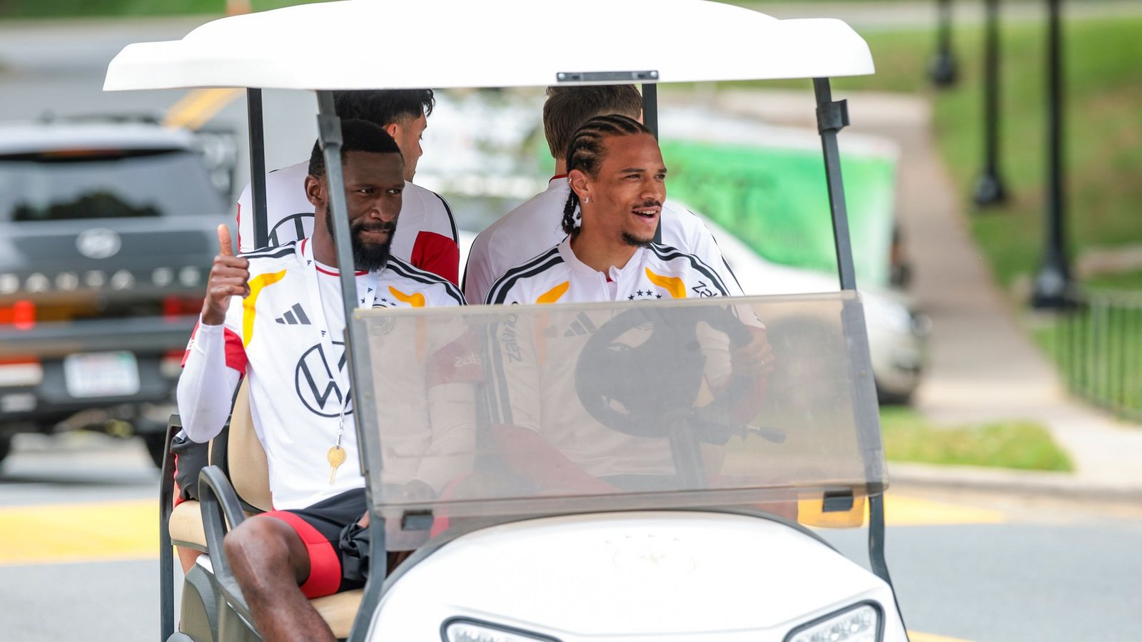Zwei Umstrittene, die sich bestens verstehen: Beifahrer Antonio Rüdiger und Fahrer Leroy Sané (r) im Golfcart auf dem Weg zum Trainingsplatz. (Archivbild)Foto: Jan Woitas/dpa