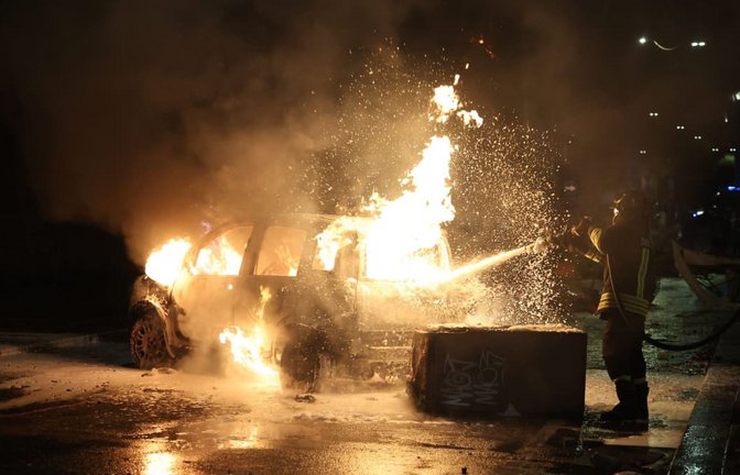 Einsatzkräfte löschen ein brennendes Auto nach Auseinandersetzungen bei Protesten in Italien<span class='image-autor'>Guido Calamosca/dpa</span>
