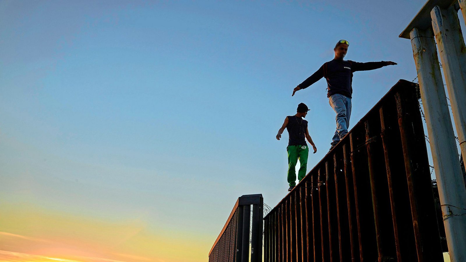 Zwei Migranten aus Mittelamerika balancieren bei Tijuana auf dem Grenzzaun zwischen Mexiko und den USA.Foto: dpa/Gregory Bull Zwei Migranten aus Mittelamerika balancieren bei Tijuana auf dem Grenzzaun zwischen Mexiko und den USA.Foto: dpa/Gregory Bull
