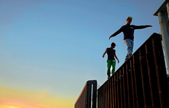 Zwei Migranten aus Mittelamerika balancieren bei Tijuana auf dem Grenzzaun zwischen Mexiko und den USA.<span class='image-autor'>Foto: dpa/Gregory Bull</span>