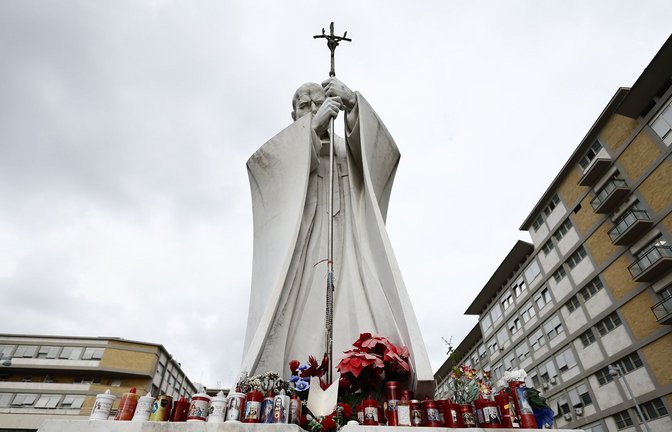 Blumen und Kerzen stehen vor einer Statue von Papst Johannes Paul II. neben der Poliklinik Agostino Gemelli in Rom, wo Papst Franziskus zur Untersuchung liegt.<span class='image-autor'>Foto: dpa/Cecilia Fabiano</span>