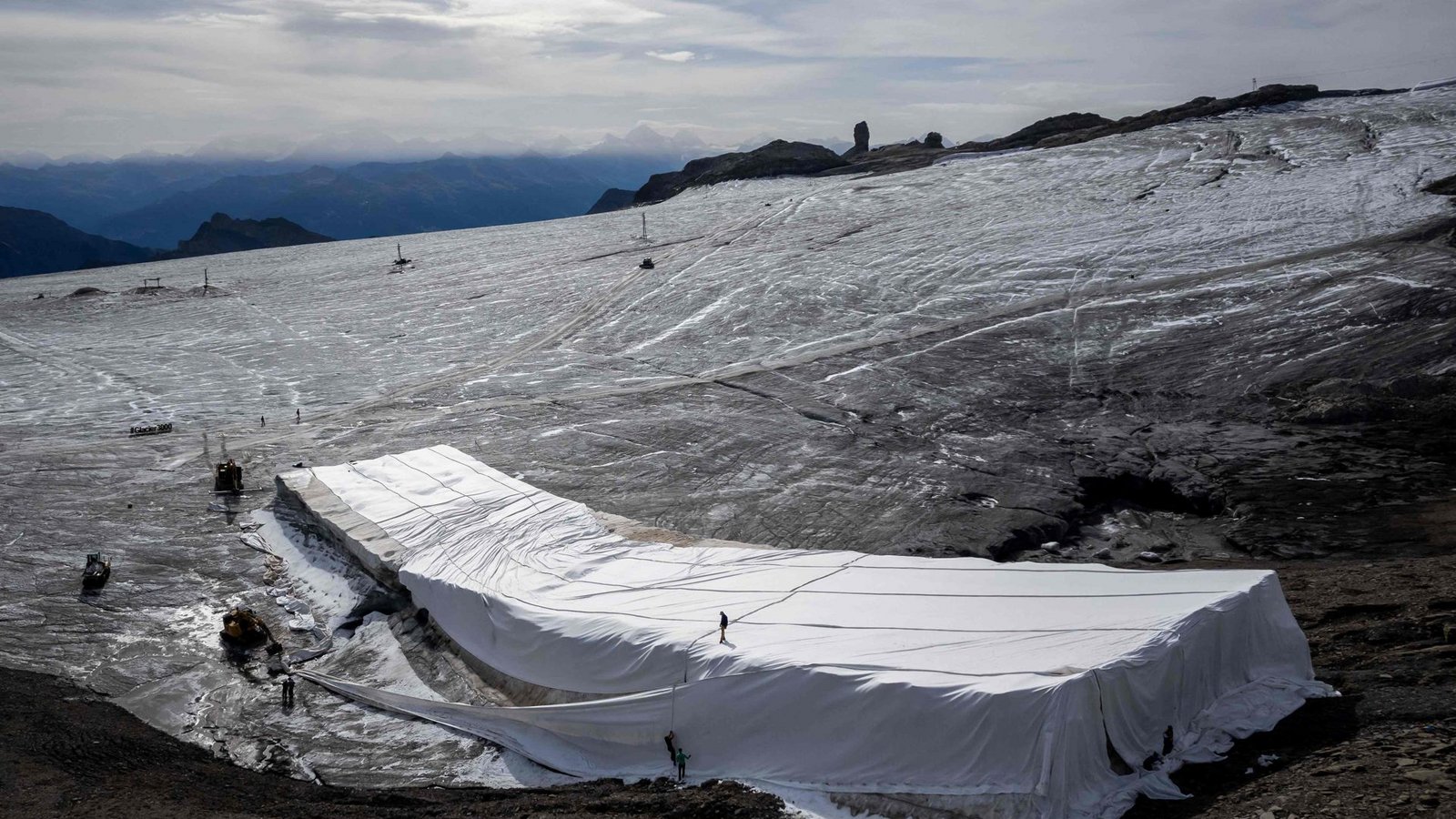 Arbeiter bedecken mit einer weißen Decke Schnee der letzen Saison auf dem Glacier 3000 in der Schweiz, um ihn vor dem Schmelzen zu schützen.Foto: AFP/FABRICE COFFRINI