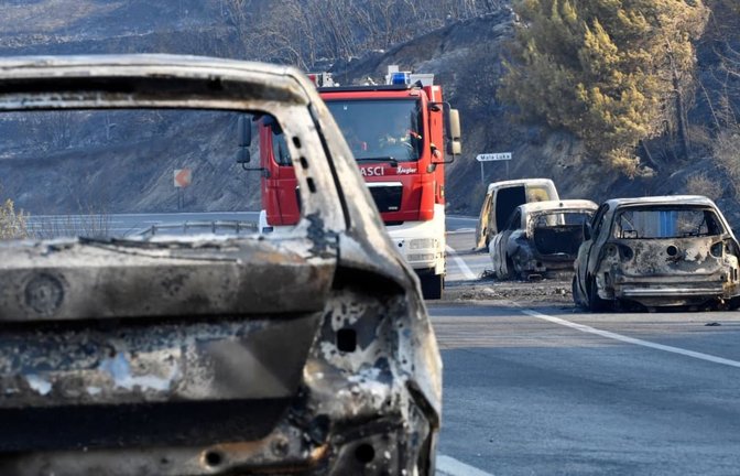 Ein Feuerwehrfahrzeug fährt nach einem Waldbrand zwischen ausgebrannten Autos hindurch.<span class='image-autor'>Josko Ponos/AP/dpa</span>