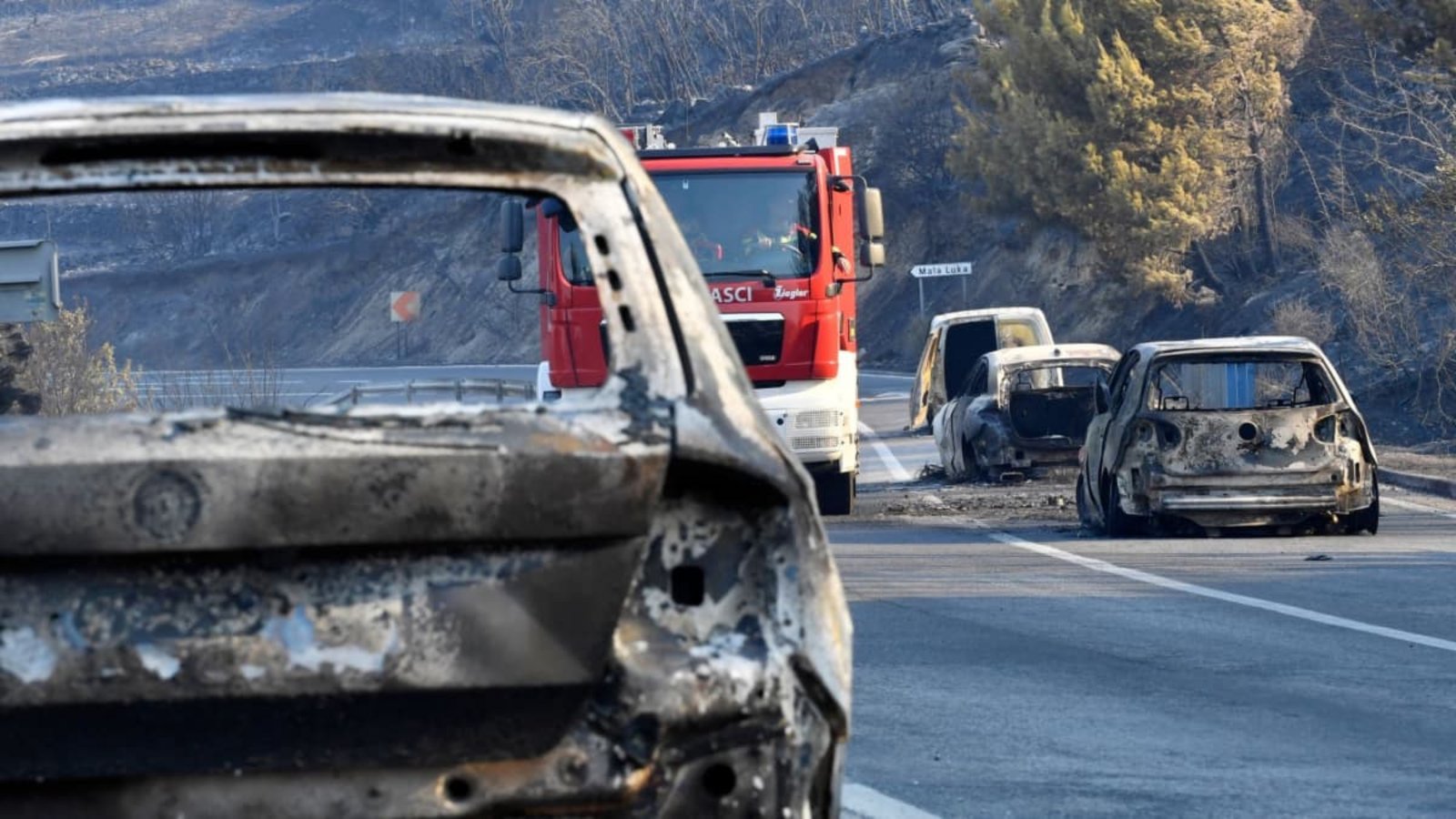 Ein Feuerwehrfahrzeug fährt nach einem Waldbrand zwischen ausgebrannten Autos hindurch.Josko Ponos/AP/dpa Ein Feuerwehrfahrzeug fährt nach einem Waldbrand zwischen ausgebrannten Autos hindurch.Josko Ponos/AP/dpa