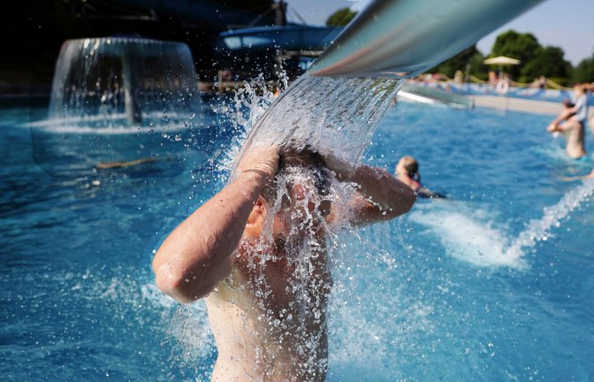Ein Mann steht bei Temperaturen von über 30 Grad im Freibad unter einer Wasserfontäne.<span class='image-autor'>Foto: Thomas Warnack/dpa/Thomas Warnack</span>