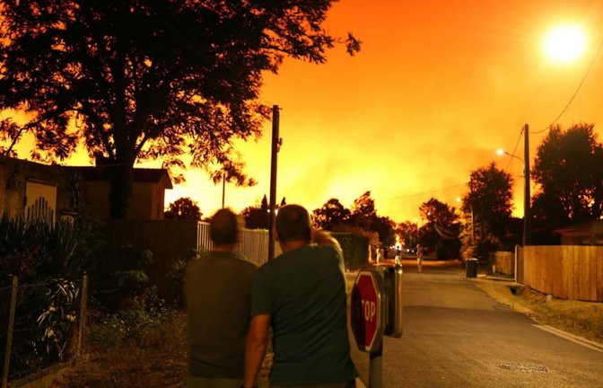 Waldbrände in Franreich aktuell: Anwohner blicken am frühen Morgen in Le Porge im Südwesten Frankreichs in den von Waldbränden erhellten Himmel.<span class='image-autor'>Romain Perrocheau/AFP/dpa</span>