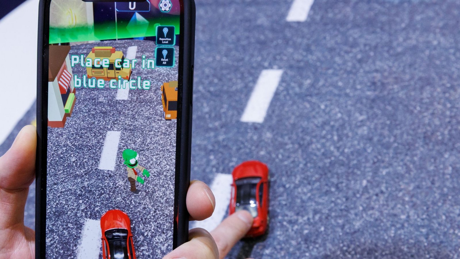Mittels Smartphone, welches ein reales Spielzeugauto mit der Kamera erfasst, wird beim Spiel "Zombie Crasher AR" von Augmented Robotics eine virtuelle Straßenszene dargestellt.Foto: Daniel Karmann/dpa