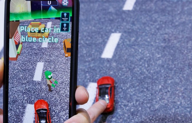 Mittels Smartphone, welches ein reales Spielzeugauto mit der Kamera erfasst, wird beim Spiel "Zombie Crasher AR" von Augmented Robotics eine virtuelle Straßenszene dargestellt.<span class='image-autor'>Foto: Daniel Karmann/dpa</span>