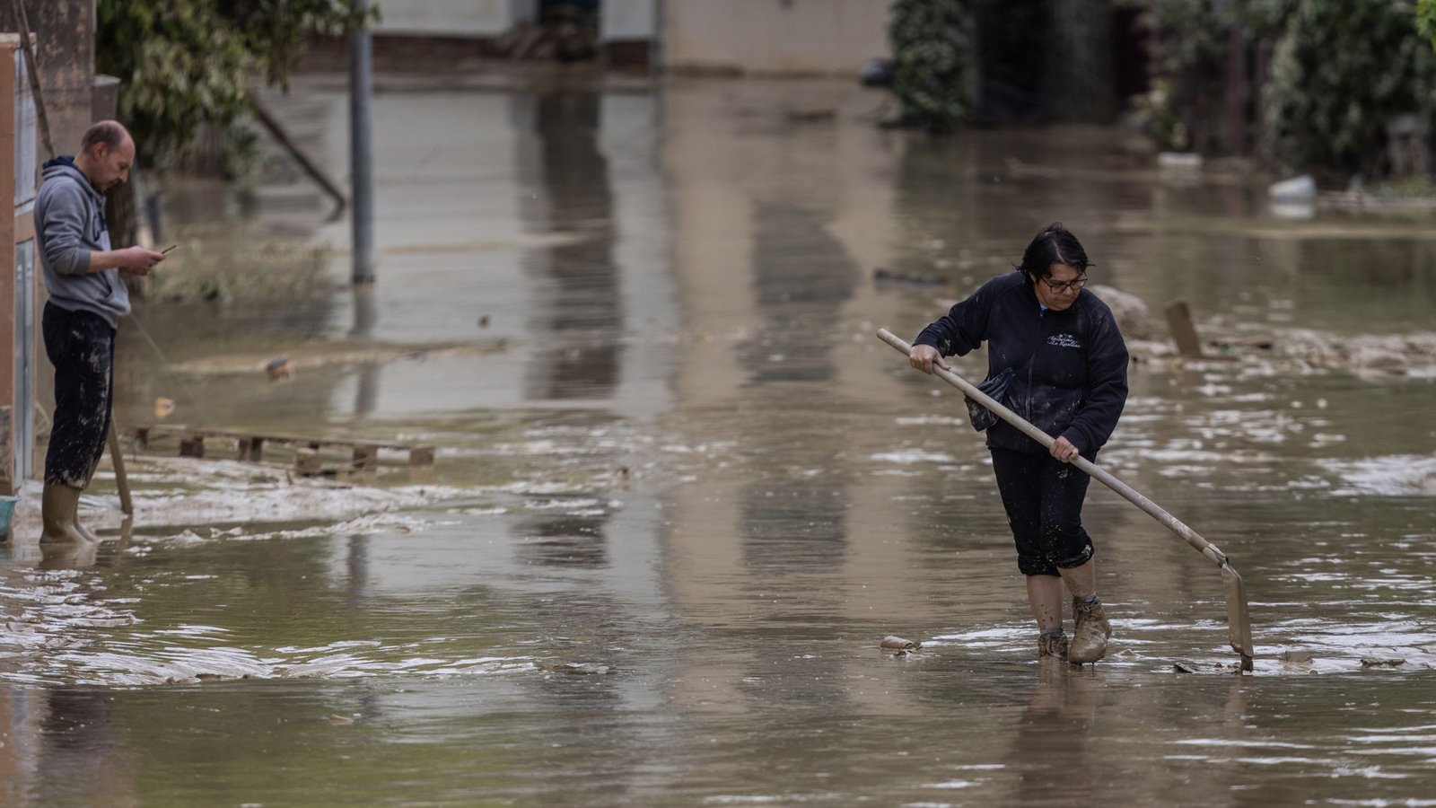 . . . . Anwohner versuchen nach Überschwemmungen eine Straße von Schlamm und Wasser zu befreien.Foto: Oliver Weiken/dpa . . . . Anwohner versuchen nach Überschwemmungen eine Straße von Schlamm und Wasser zu befreien.Foto: Oliver Weiken/dpa