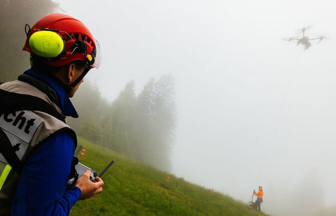 Ein Drohnenpilot der Bergwacht sieht zu, wie ein Flughelfer der Bergwacht eine Übungslast von der Seilwinde einer Lastendrohne abhängt.<span class='image-autor'>Foto: Philipp von Ditfurth/dpa</span>