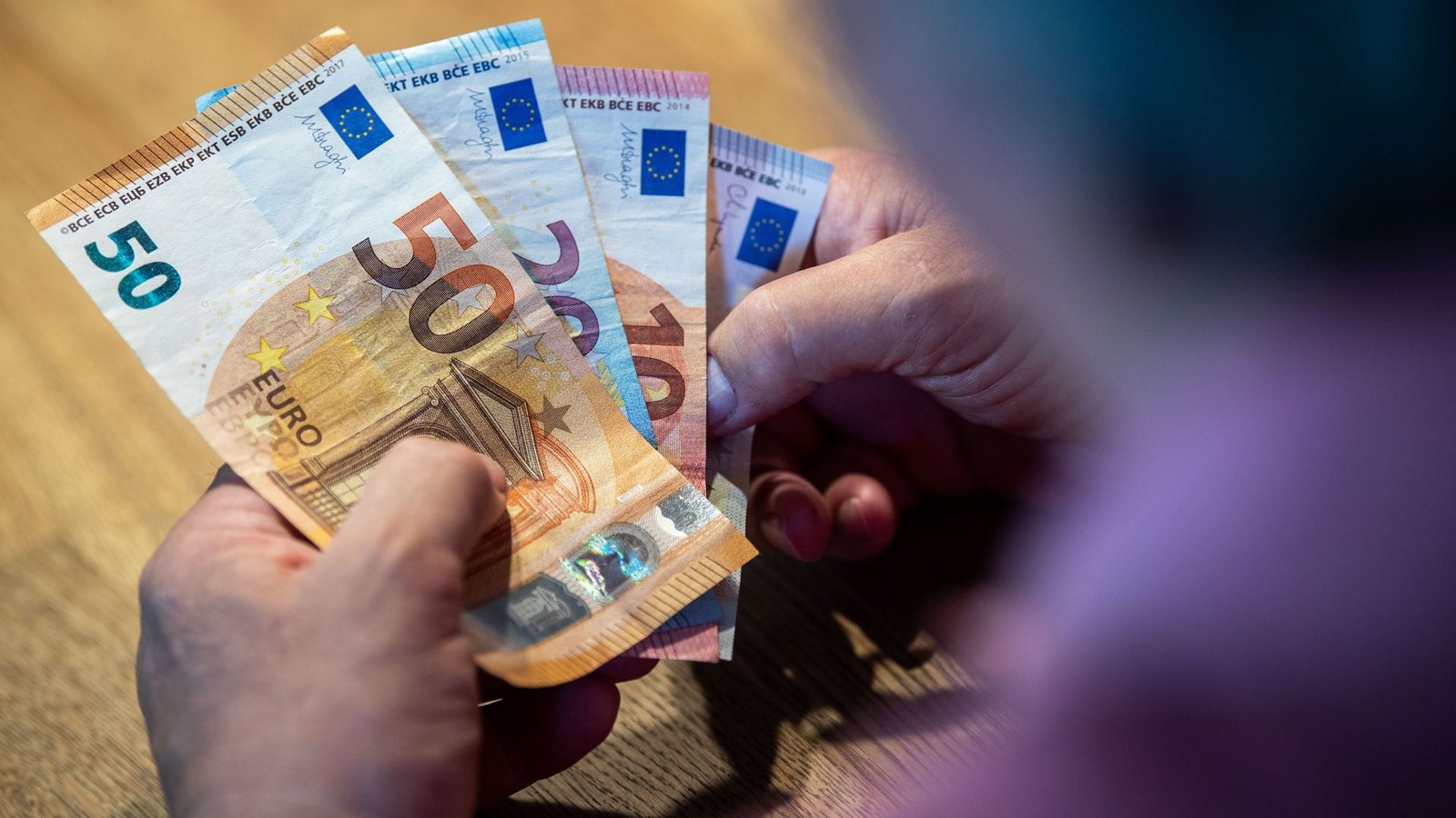 Ein älterer Mann sitzt an einem Tisch und zählt Geld.Foto: dpa/Lino Mirgeler