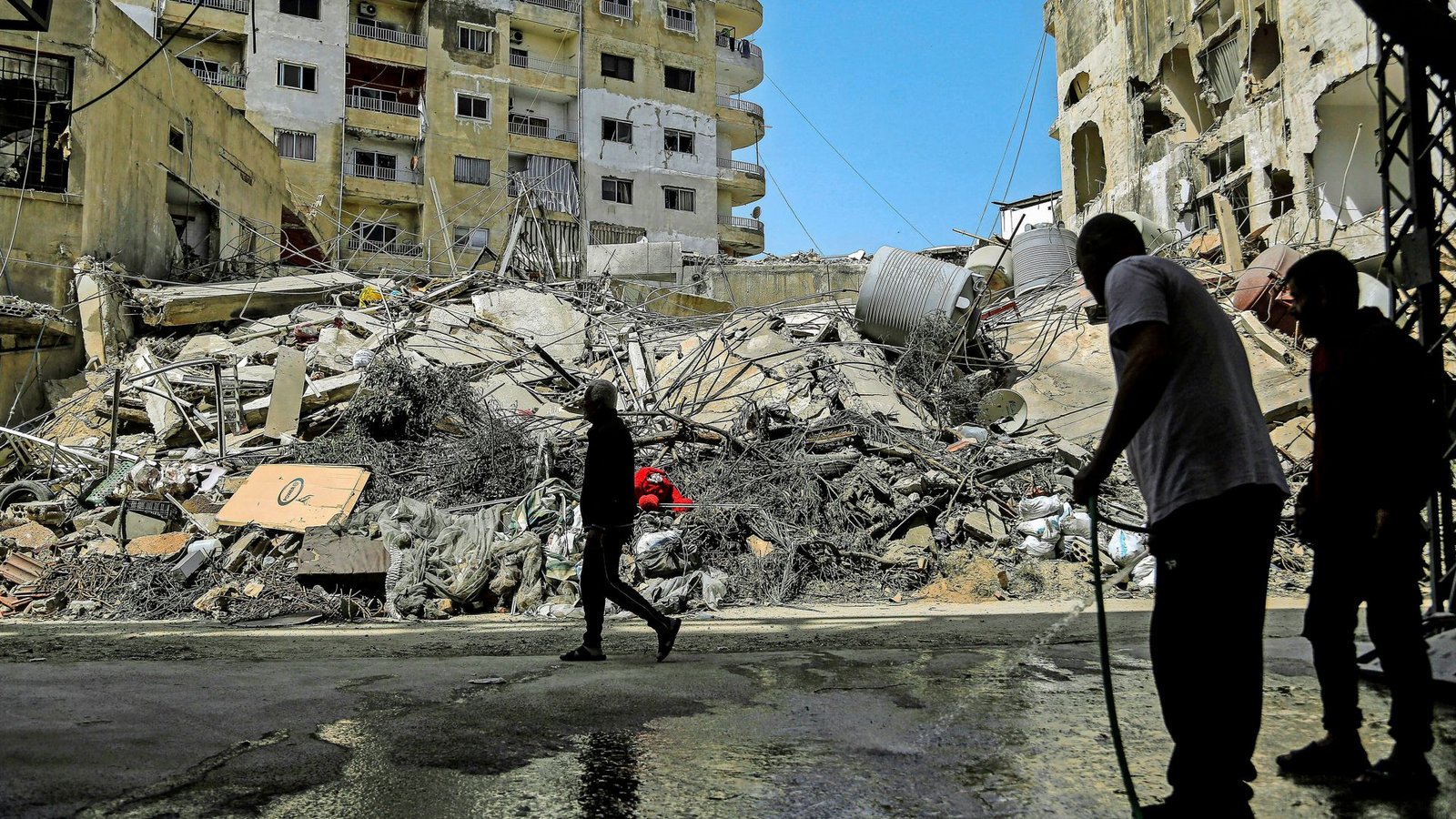 Ein Libanese spritzt mit einem Schlauch eine Straße vor den zerstörten Gebäuden ab, die von israelischen Luftangriffen  getroffen wurden (Archivfoto).Foto: Marwan Naamani/dpa/Marwan Naamani