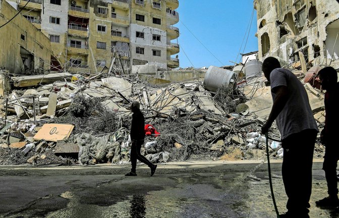 Ein Libanese spritzt mit einem Schlauch eine Straße vor den zerstörten Gebäuden ab, die von israelischen Luftangriffen  getroffen wurden (Archivfoto).<span class='image-autor'>Foto: Marwan Naamani/dpa/Marwan Naamani</span>