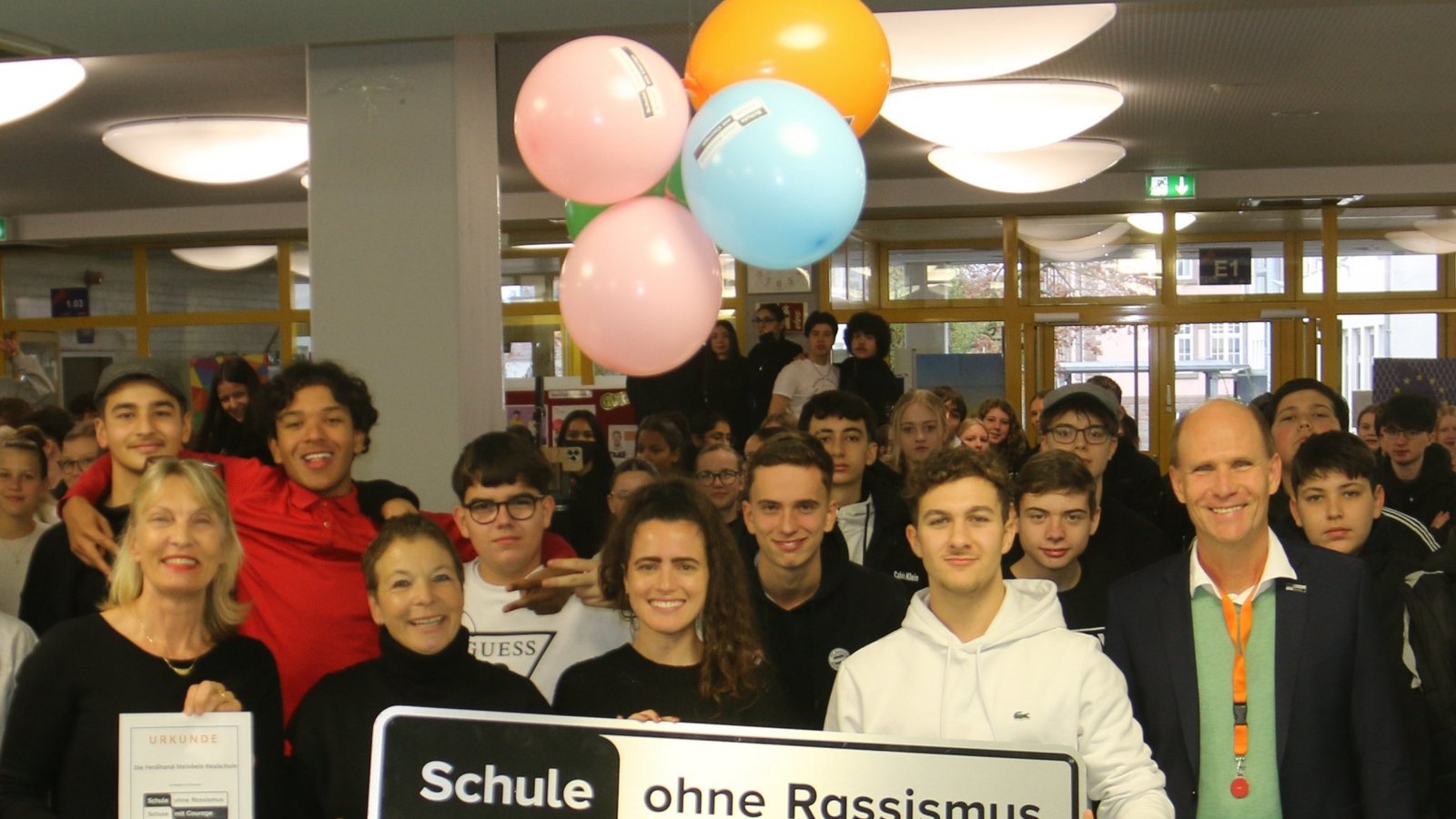 Ein Teil der Schulgemeinschaft bei der Überreichung der Urkunde, welche die Schulleiterin Claudia Süß-Räuchle in Händen hält. Am Schild (von links) die Lehrerinnen Claudia Queißer, Sophie Nowitzki und Schülersprecher Angelos. Daneben Landeskoordinator Dr. Niels Joeres und rechts im Bild Bernhard Freckmann von der KZ-Gedenkstätte.  Foto: Rücker