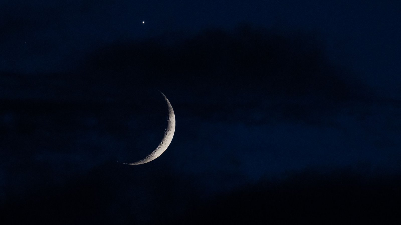 Der sichelförmige Mond wird am Abend hinter Wolken über Köln von der Venus (oben) begleitet.Foto: Rolf Vennenbernd/dpa