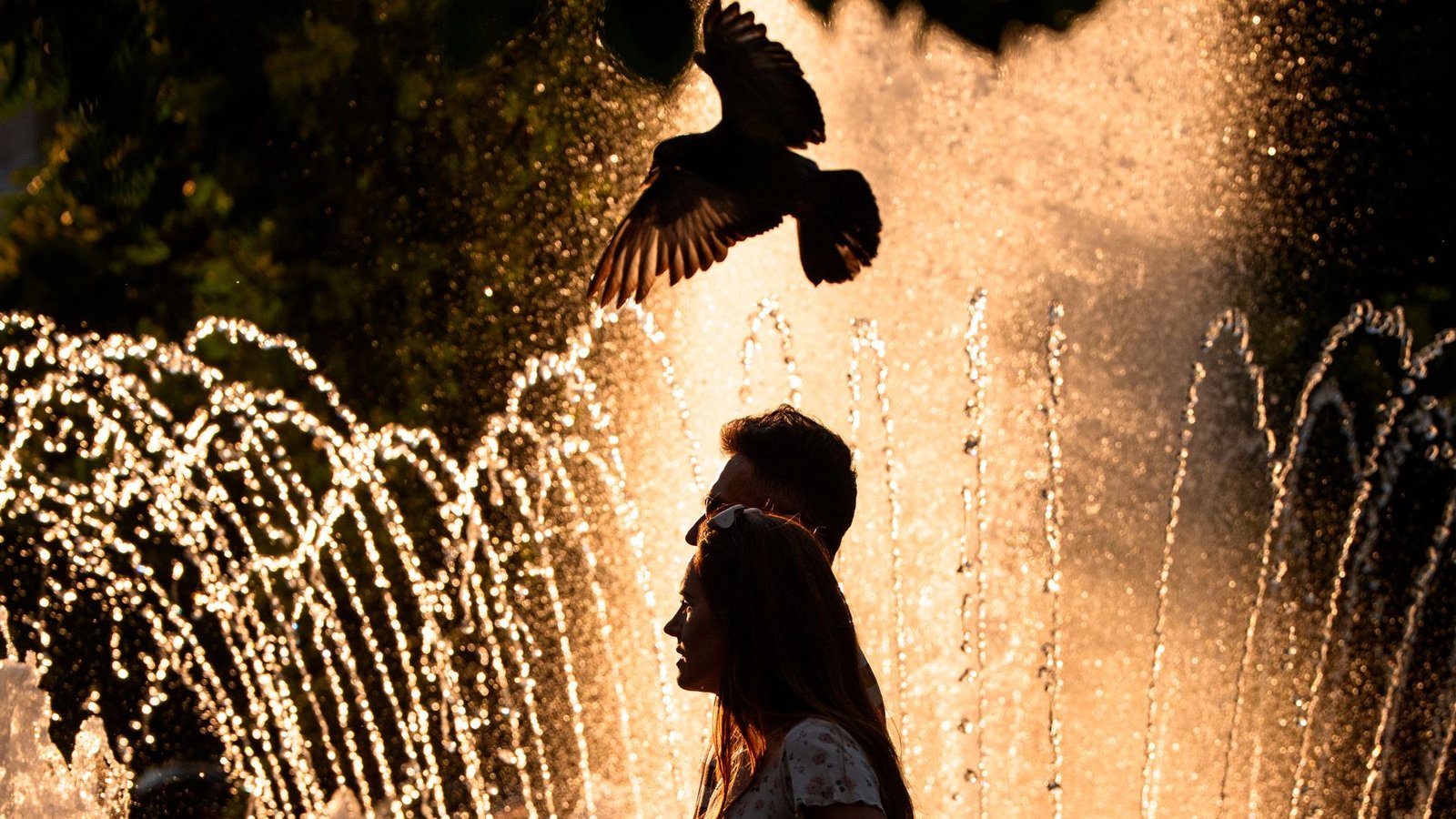 Ein Paar geht an einem Springbrunnen in Bukarest vorbei, während der nationale Wetterdienst für Teile des Landes in den kommenden Tagen eine Hitzewarnung der Stufe "Rot" herausgegeben hat.Foto: Andreea Alexandru/AP/dpa Ein Paar geht an einem Springbrunnen in Bukarest vorbei, während der nationale Wetterdienst für Teile des Landes in den kommenden Tagen eine Hitzewarnung der Stufe "Rot" herausgegeben hat.Foto: Andreea Alexandru/AP/dpa