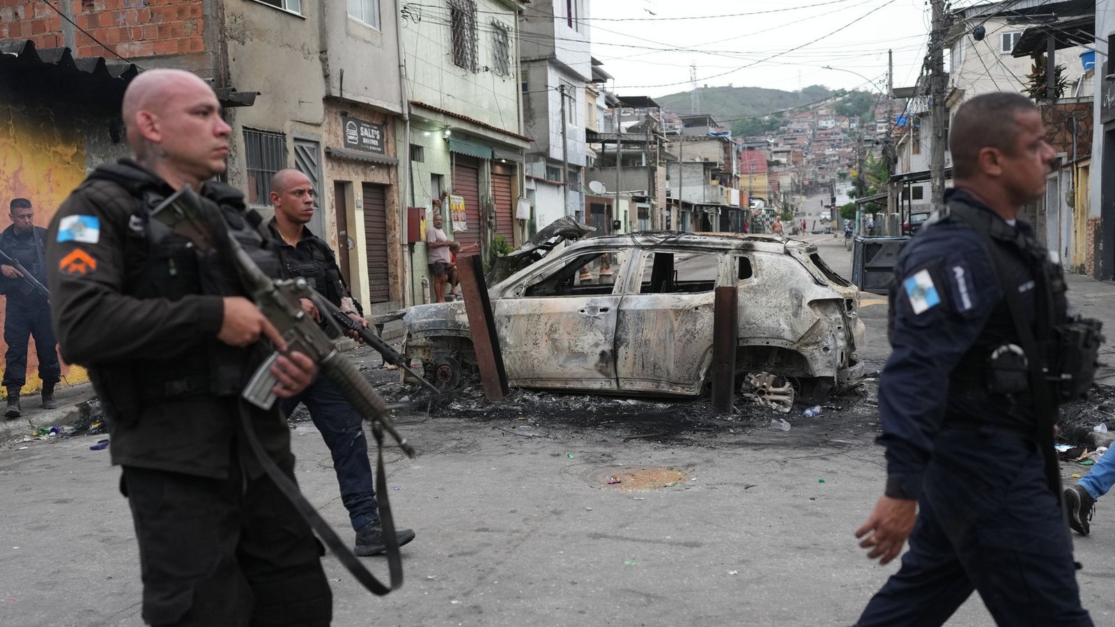 Favela „Complexo Alemao“: Polizisten gehen am Tag danach an einem verbrannten Auto vorbei.Foto: dpa/Silvia Izquierdo Favela „Complexo Alemao“: Polizisten gehen am Tag danach an einem verbrannten Auto vorbei.Foto: dpa/Silvia Izquierdo