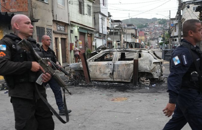 Favela „Complexo Alemao“: Polizisten gehen am Tag danach an einem verbrannten Auto vorbei.<span class='image-autor'>Foto: dpa/Silvia Izquierdo</span>