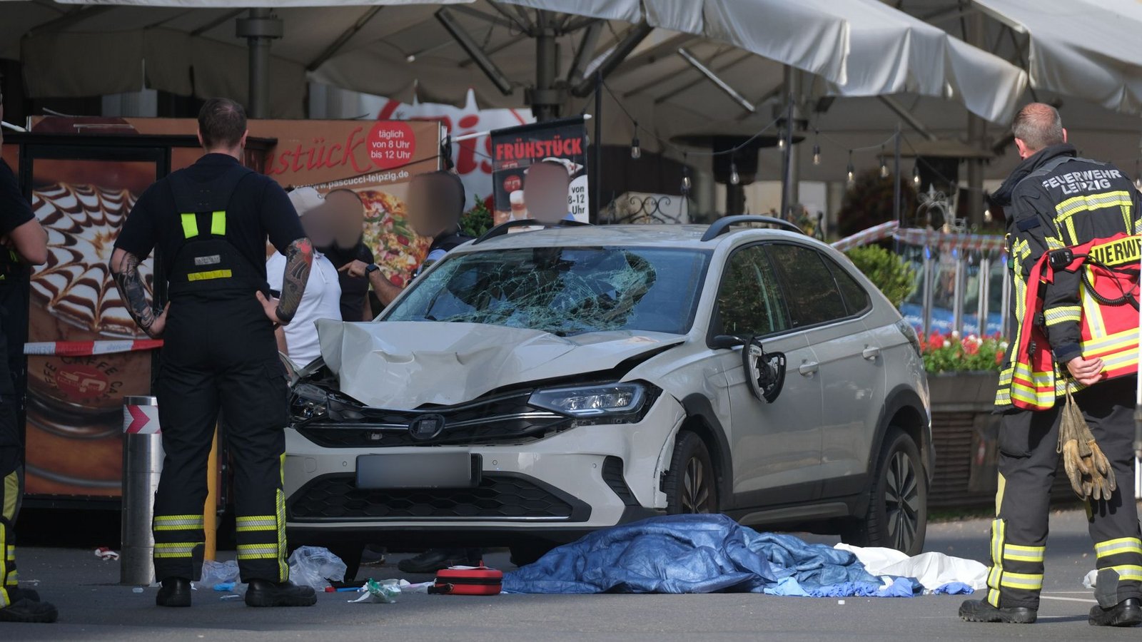 Einsatzkräfte und weitere Personen stehen um ein beschädigtes Auto. In Leipzig ist ein Auto in mehrere Menschen gefahren.Foto: Sebastian Willnow/dpa/Sebastian Willnow Einsatzkräfte und weitere Personen stehen um ein beschädigtes Auto. In Leipzig ist ein Auto in mehrere Menschen gefahren.Foto: Sebastian Willnow/dpa/Sebastian Willnow