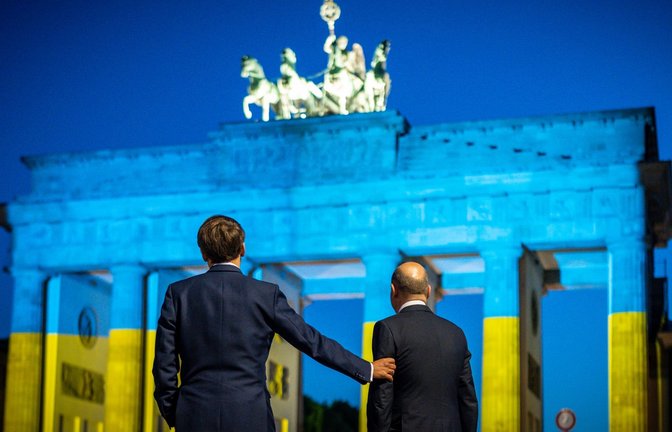 Bundeskanzler Olaf Scholz (r) und Frankreichs Präsident Emmanuel Macron blicken auf das Brandenburger Tor, das in den ukrainischen Nationalfarben erstrahlt.<span class='image-autor'>Foto: Michael Kappeler/dpa</span>
