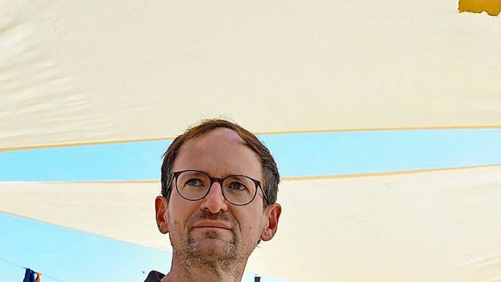 Bastian Schröter von der Hochschule für Technik beschäftigt sich mit dem Kühlbedarf Stuttgarts. Hier sitzt er unter einem Sonnensegel am Marienplatz.Foto: Lichtgut/Max Kovalenko
